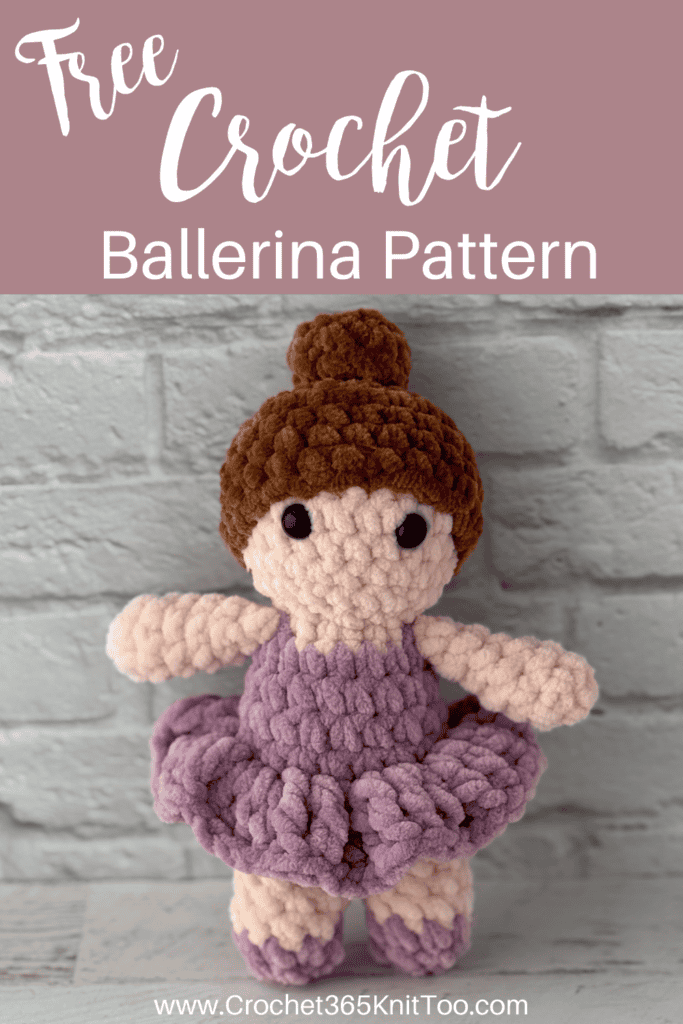 crochet ballerina with brown hair in purple dress standing in front of brick wall