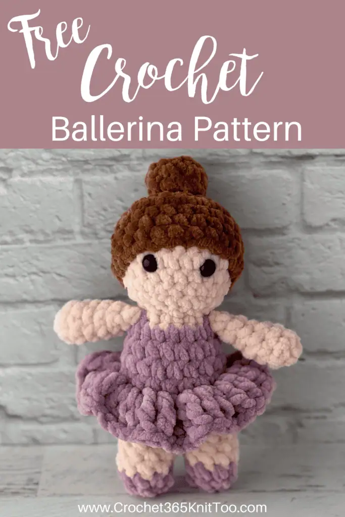 crochet ballerina with brown hair in purple dress standing in front of brick wall