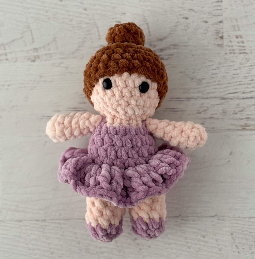 crochet ballerina with brown hair in purple dress on white wood table