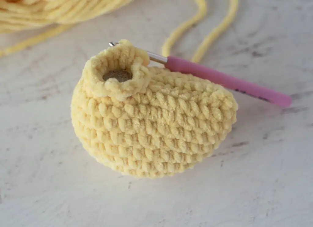 Crochet duck out of yellow yarn on white wood background