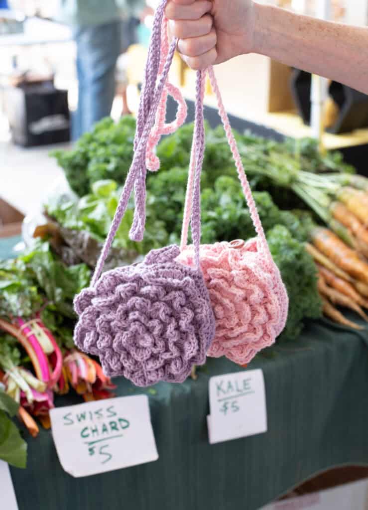 Purple and Pink crochet market bags in front of produce at a market