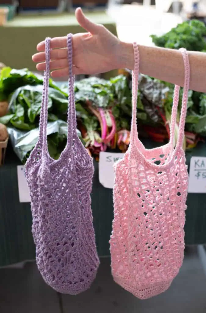 Purple and Pink crochet market bags in front of produce at a market