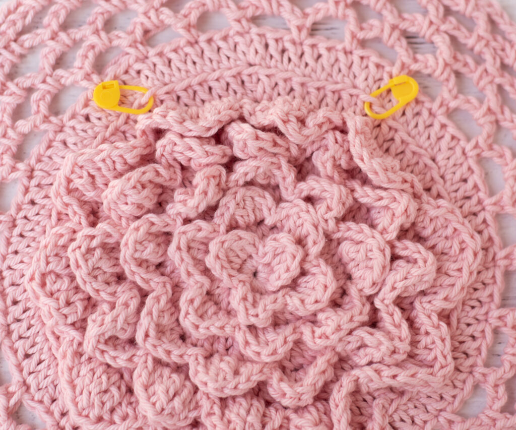 Pink floral crochet market bag bottom with two yellow stitch markers
