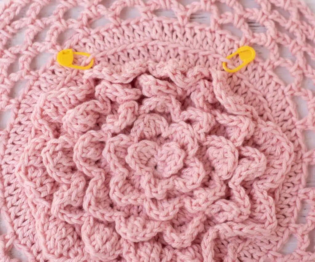 Pink floral crochet market bag bottom with two yellow stitch markers