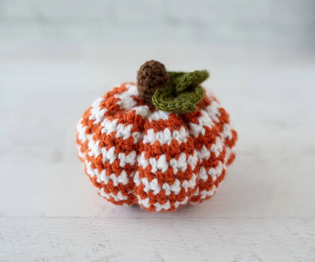 crochet houndstooth patterned pumpkin in orange and white yarn with brown stem and green leaves