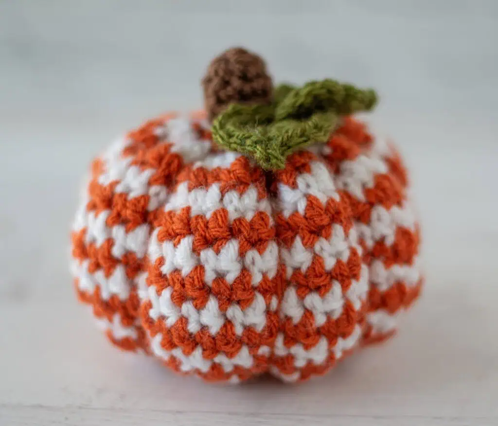 crochet houndstooth patterned pumpkin in orange and white yarn with brown stem and green leaves