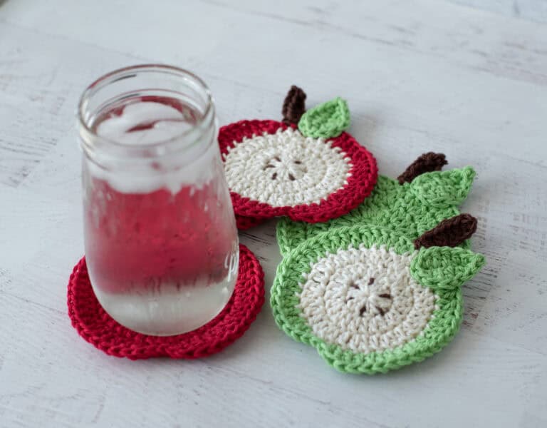 Crochet red apple coasters with glass of water. One coaster is a slide of apple with seeds, the rest are red.