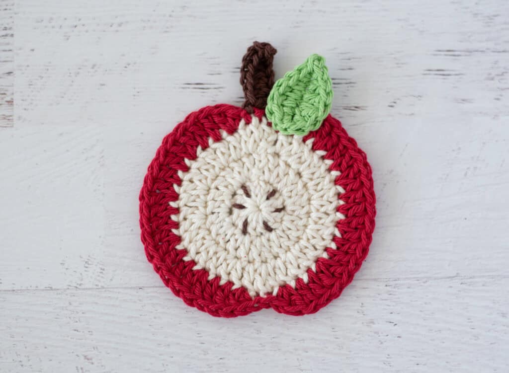 Red slice apple coaster in red and cream with brown stem and leaf.